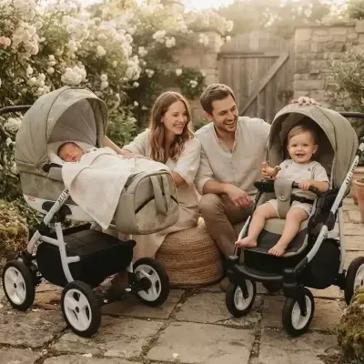 Dois carrinhos de bebé verdes com bebés e casal num jardim de pedra