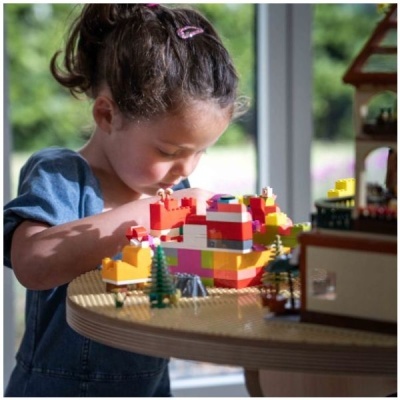 Menina a brincar com blocos de construção coloridos numa mesa redonda de madeira