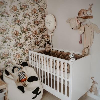 Berço branco de madeira com proteção trançada castanha e cadeira bean bag com padrão de rosto de cão