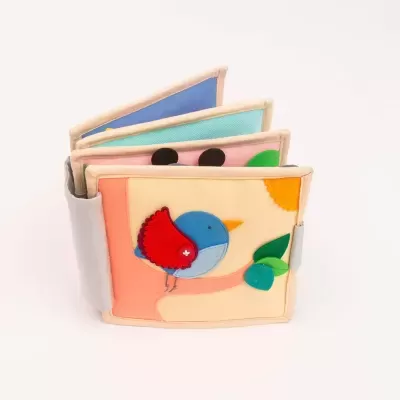 Livro infantil em tecido colorido com pássaro e elementos em relevo