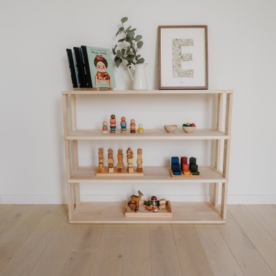 Estante de madeira clara com livros, bonecos e um quadro com a letra E