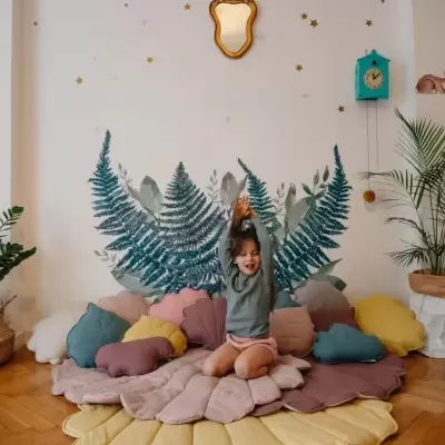 Tapete almofadado colorido em forma de flor com criança sentada no centro e parede decorada ao fundo