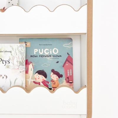 Estante branca com livros infantis, destaque para livro azul com crianças e título em polaco.