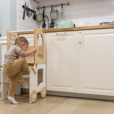 Bebé com torre de aprendizagem de madeira numa cozinha branca