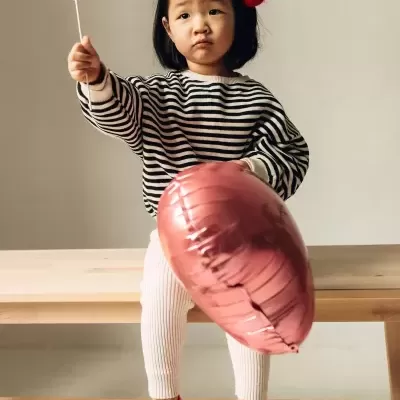 Criança sentada com camisola riscada e balão coração rosa
