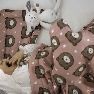 Bebé a dormir com manta de ursinhos e pelúcia branca no berço