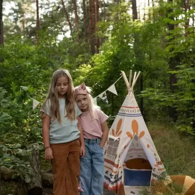 Duas crianças são observadas perto de uma tenda tipi com padrões em floresta