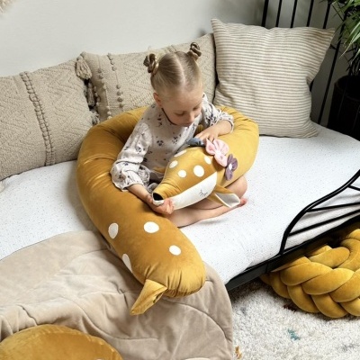Criança com almofada em forma de veado em sofá com almofadas neutras num ambiente acolhedor.