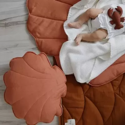 Tapete e almofada terracota com bebé deitado em cobertor branco
