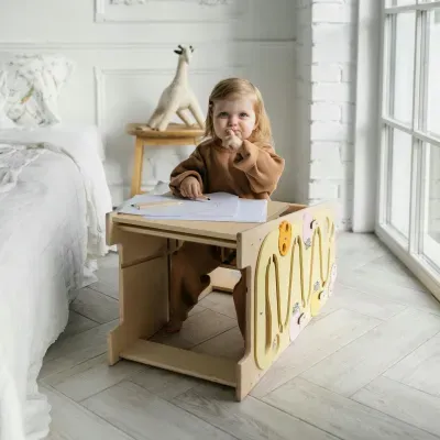Criança a desenhar numa mesa infantil de madeira com painéis coloridos