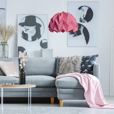 Sala de estar com sofá cinzento claro, mesa de centro, candeeiro rosa e quadros artísticos em preto e branco