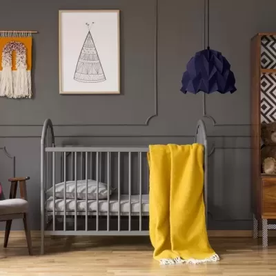 Quarto de bebé com berço cinzento, cadeira com almofada rosa, cobertor amarelo e prateleira com ursos de peluche