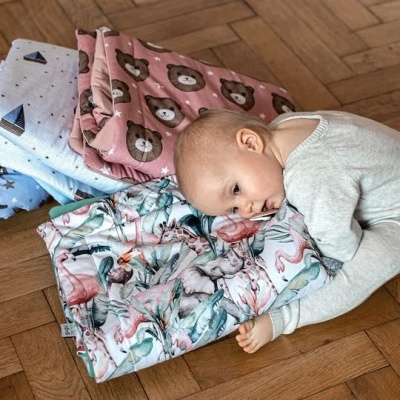 Bebé deitado sobre mantas com padrões de ursos e flamingos no chão de madeira