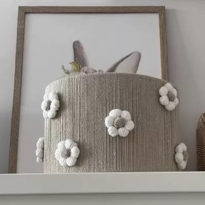 Cesto redondo de tecido bege com flores brancas à frente de quadro com orelhas de coelho