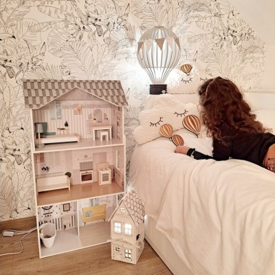 Casa de bonecas branca e cinzenta junto a cama e papel de parede decorativo.