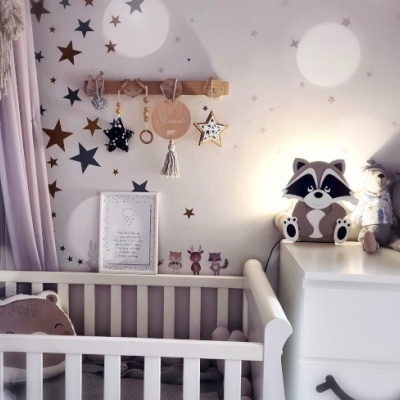 Quarto de bebé decorado com berço branco, estrelas na parede e candeeiro de guaxinim