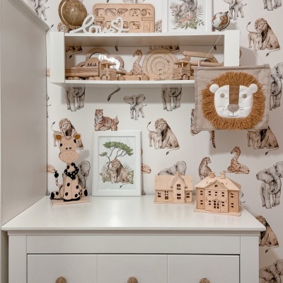 Cômoda branca com gavetas em ambiente infantil decorado com papel de parede de animais selvagens e brinquedos de madeira
