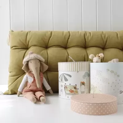 Almofada verde, peluche de elefante vestido, caixas decorativas redondas sobre mesa branca