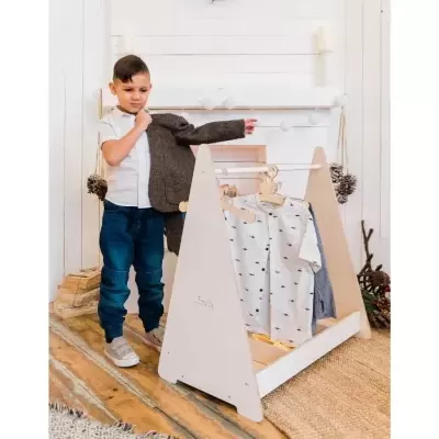 Menino a experimentar casaco cinzento ao lado de cabide de madeira com roupas