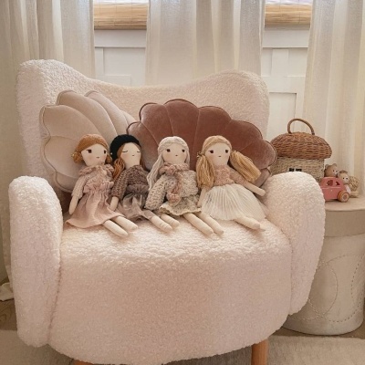 Cadeira branca felpuda com almofadas florais e quatro bonecas de pano sentadas.
