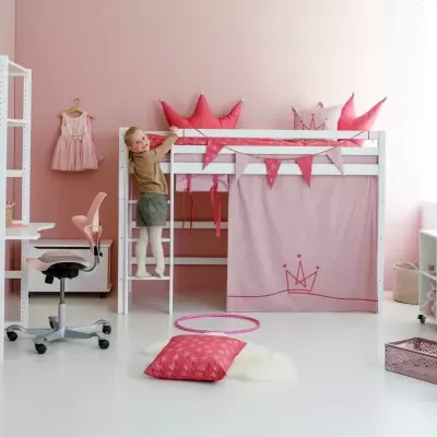 Quarto infantil com cama alta branca e decoração rosa, cadeira ergonómica e secretária brancas, almofadas, cortina com coroa, brinquedos e prateleiras.
