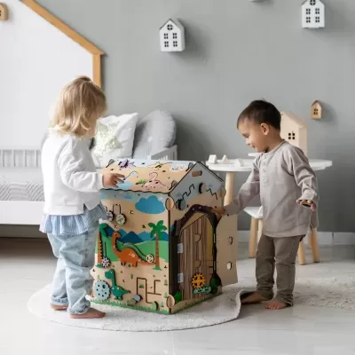 Crianças a brincar com uma casa de madeira colorida com dinossauros e plantas