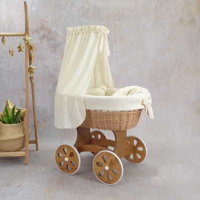 Berço de bebé em carrinho de madeira e vime com cobertura creme e almofadas acolchoadas num ambiente de parede cinza texturizada