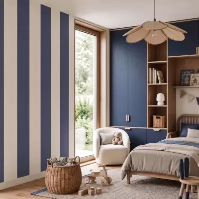 Quarto infantil com móveis em madeira clara e azul escuro, cama com almofadas, poltrona branca, candeeiro flores e brinquedos de madeira.