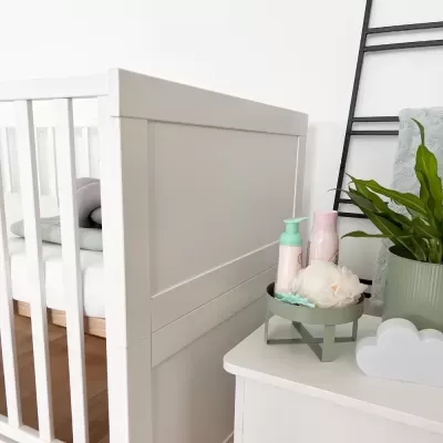 Berço branco e mesa com frascos, esponja e planta