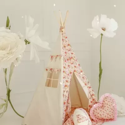 Tenda de brincar bege com estampa floral rosa e almofadas decorativas junto a flores brancas grandes