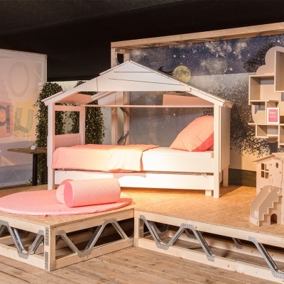 Cama infantil branca em madeira em formato de casinha com roupa de cama cor de rosa num cenário com padrão estrelado
