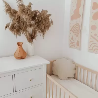 quarto minimalista com cômoda branca, vaso com flores secas, berço claro com almofada de flor e painéis decorativos na parede