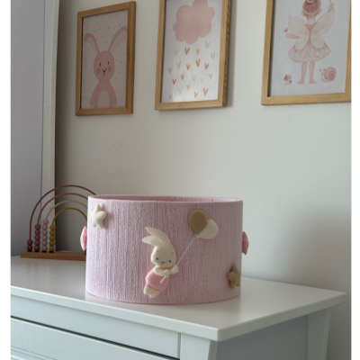 Cesto rosa decorado com coelho e balões, sobre cómoda branca, com quadros infantis atrás