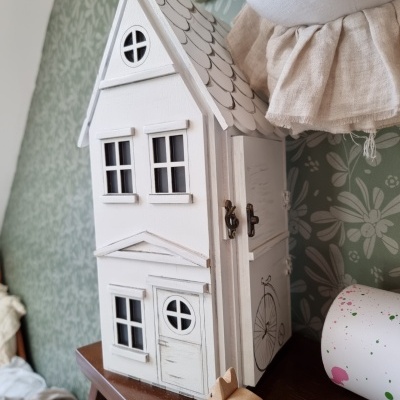 Miniatura de casa branca em madeira com janelas e porta simuladas sobre móvel de madeira escura