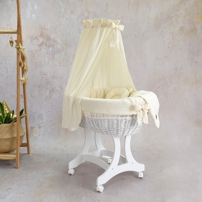 Berço de bebé redondo em vime branco com dossel amarelo pálido, sobre suporte de madeira e rodas, em ambiente neutro