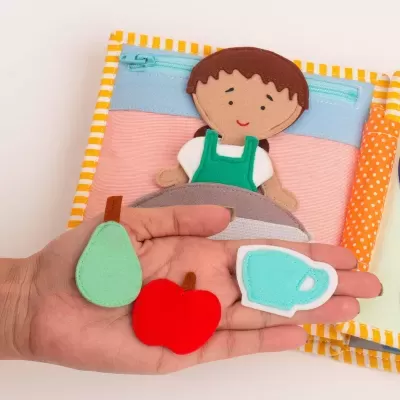 Livro de tecido com figura de menino e peças de frutas e chávena