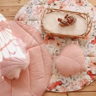 Tapete infantil redondo floral, almofadas rosa em forma de concha e folha, cesto de verga com boneco