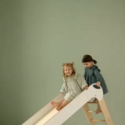 DuAS crianças em escorrega infantil de madeira clara em fundo verde claro