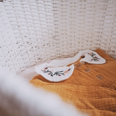 Roupa de bebé mostarda com gola branca bordada num cesto de vime branco