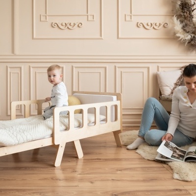 Cama infantil de madeira clara com grades e decoração acolhedora num quarto aconchegante.
