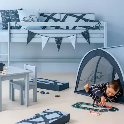 Quarto infantil com cama alta branca, tenda azul e menino a brincar com carrinhos