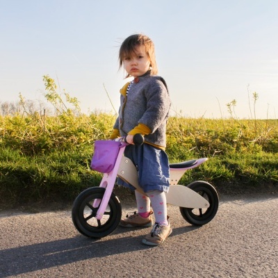 Criança numa bicicleta de equilíbrio de madeira com detalhes rosa ao ar livre