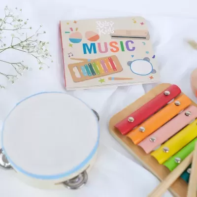 Conjunto infantil musical com xilofone, pandeiro e livro com texto 'Busy Kids MUSIC'.