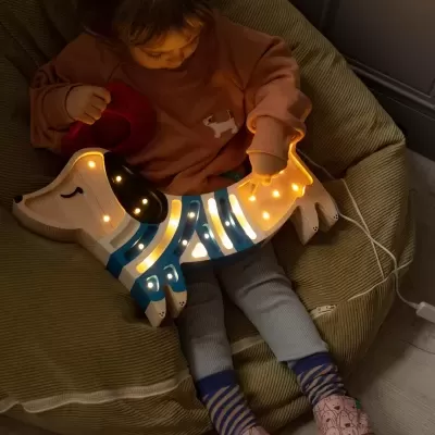Criança sentada com candeeiro de cão em madeira iluminado, roupa confortável e pantufas com padrão de cães.