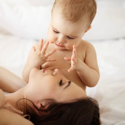 Bebé loiro-avermelhado abraçando mulher numa cama com lençóis brancos