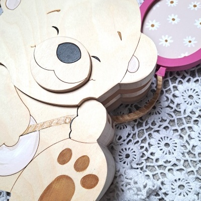 Produto de madeira em forma de urso com lupa rosa e croché branco ao fundo