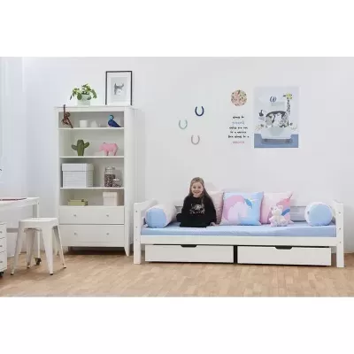 Quarto infantil com cama branca, almofadas de unicórnio e estante branca com decoração.