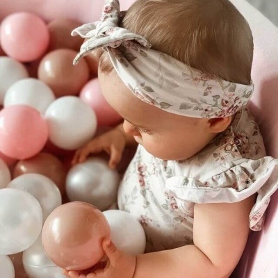 Bebé com vestido e faixa de cabelo florais sentada entre bolas de plástico coloridas