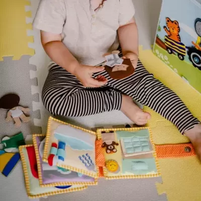 Criança a brincar com brinquedos de pano e madeira sentada num tapete de EVA