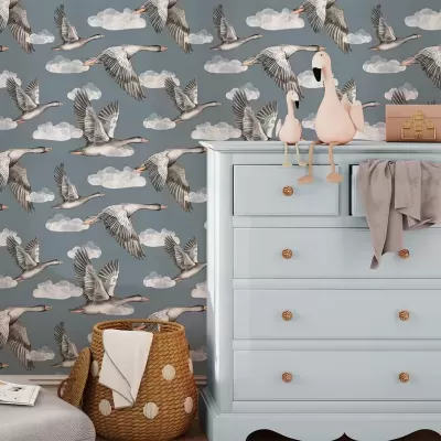 Papel de parede com gansos em voo azul cinzento e cômoda azul claro com peluches de aves cor-de-rosa e cesta de vime.